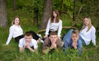 A group of young adults posing together on grass in a forest setting.